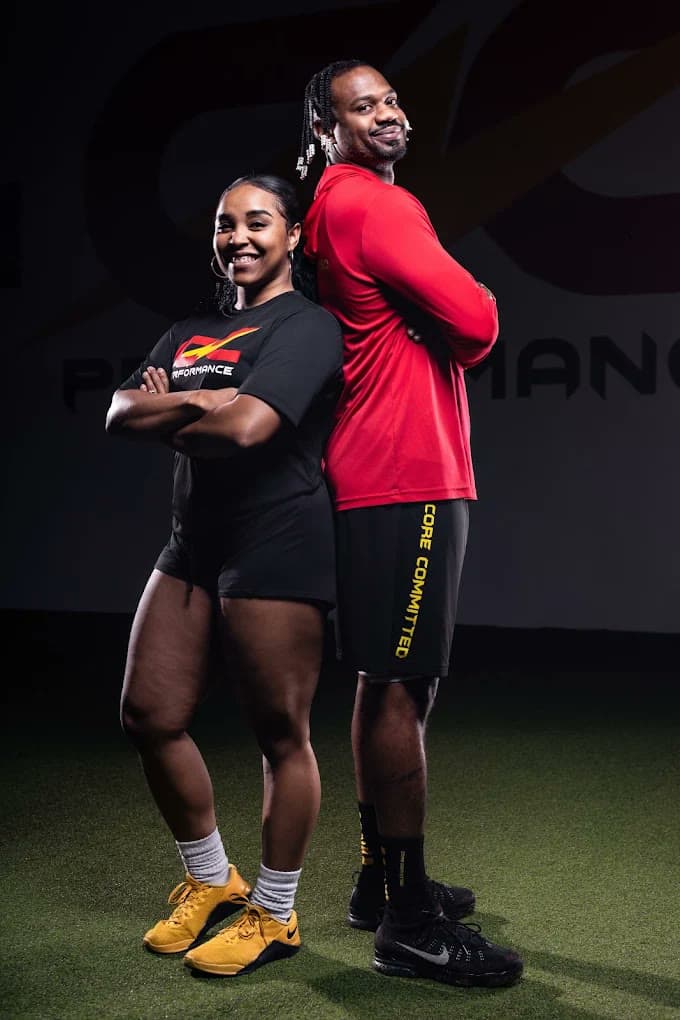 Coach Coop and Coach Candice back to back in front of the CNC Performance wall