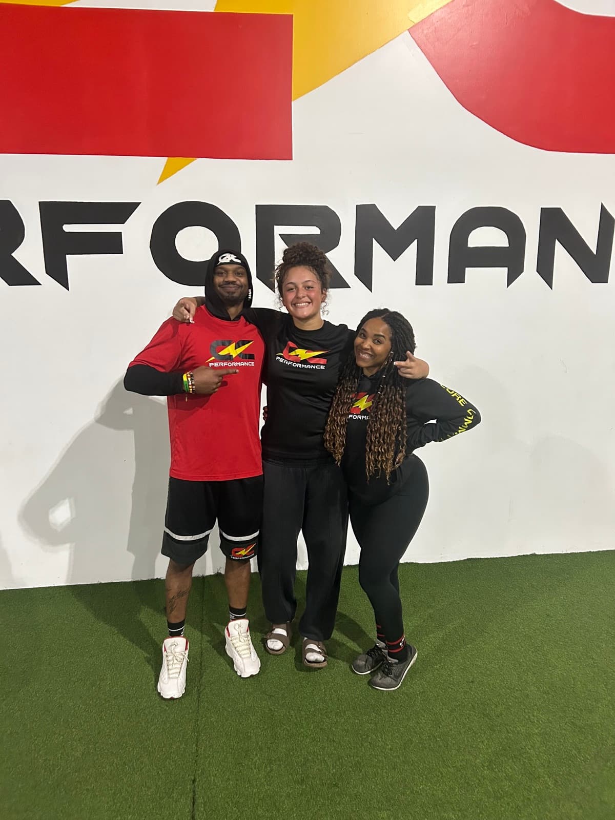 Coach Coop and Coach Candice with a CNC athlete in front of the CNC Performance wall